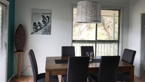 A dining area with a wooden table and chairs, a hanging light fixture, a wall-mounted artwork, and a window with blinds.