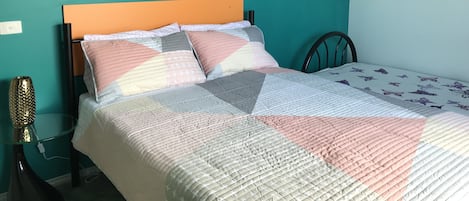 Een bed met een sprei, een houten hoofdbord en een bloemschilderij aan de muur.