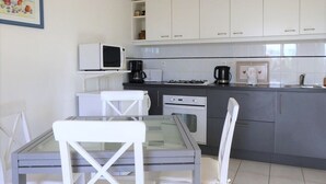 Een kleine keuken met witte kastjes, een magnetron, een koffiezetapparaat en een gasfornuis.