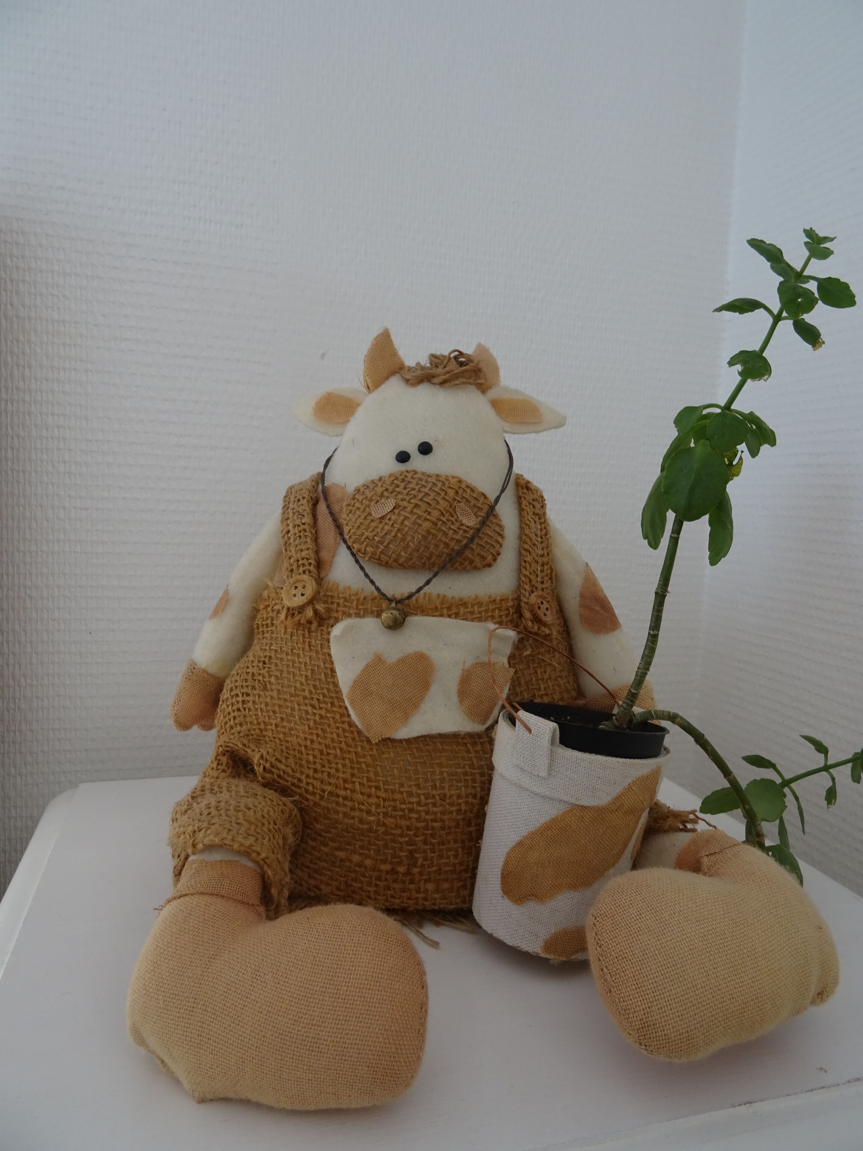 Ein plüschiges Giraffen-Spielzeug sitzt auf einer weißen Oberfläche, neben ihm ein Blumentopf.