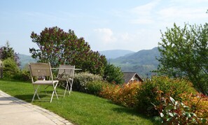 Ein Garten mit Bergblick, ein kleines Haus und zwei Stühle auf einem gepflasterten Weg.
