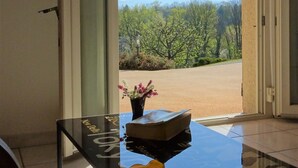 Een kamer met een glazen tafel, een gele paraplu en uitzicht op bomen en bergen.