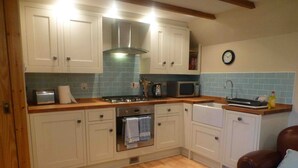 A kitchen with white cabinets, a stainless steel range hood, a microwave, a sink, and a clock on the wall.