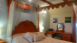 A bedroom with a canopy bed, a wooden dresser, a mirror, and two wall-mounted lamps.