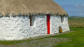 A traditional thatched-roof house with a white exterior, a red door, and a chimney.