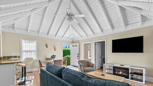 Ein geräumiges Wohnzimmer mit hoher Decke, Kamin, Fernseher und Essbereich mit Tisch und Stühlen.