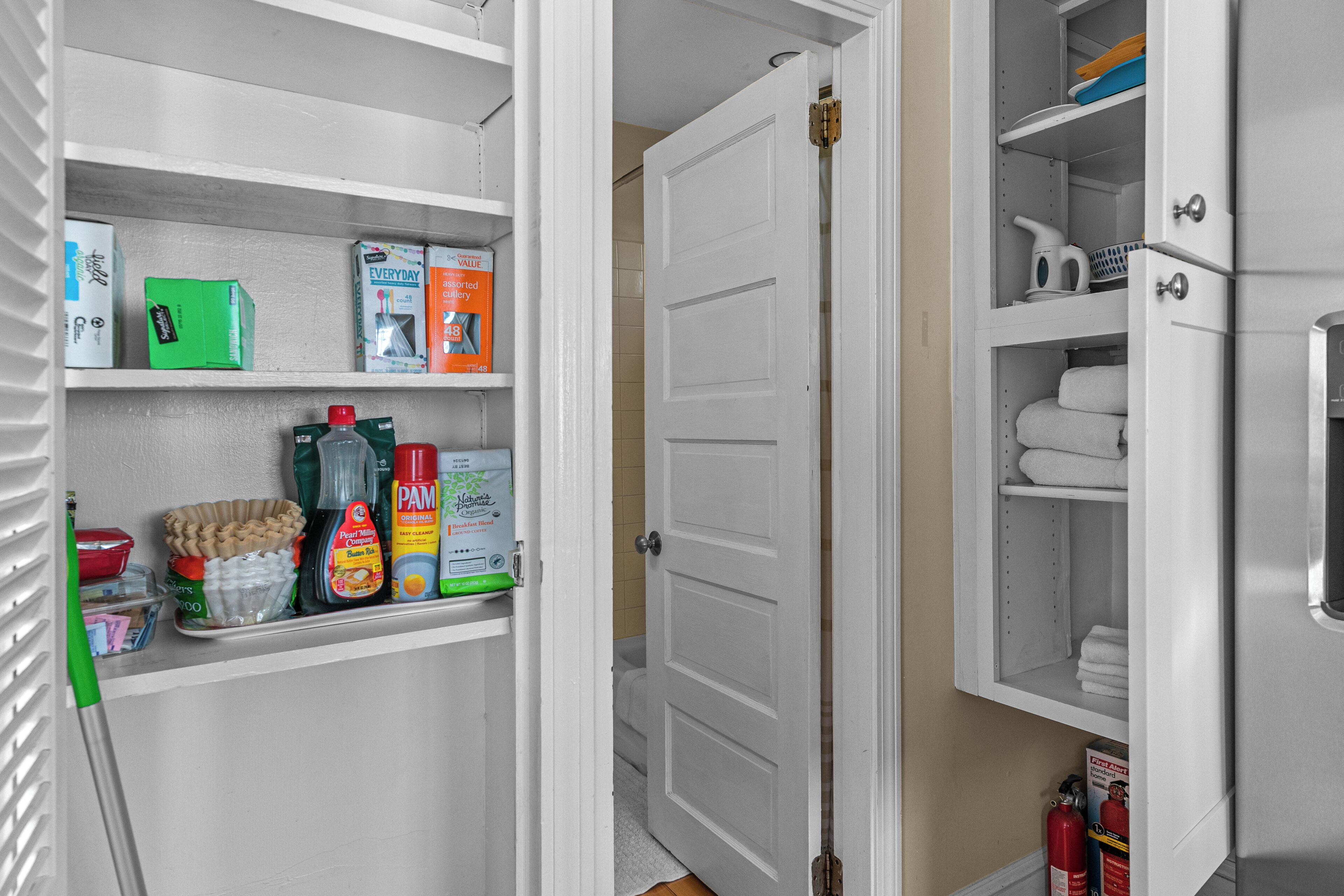 A kitchen with white cabinets, a countertop with cleaning supplies, and a door leading to a bathroom.