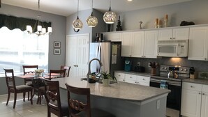 Una cocina moderna con armarios blancos, una isla central, electrodomésticos de acero inoxidable e iluminación colgante.