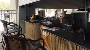 Zona de bar al aire libre con mostrador, sillas y refrigerador.