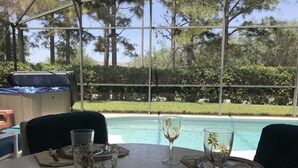 Mesa para dos con vista a una piscina y árboles al fondo.