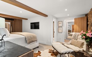 A modern bedroom with a bed, a bench, and a desk. There is a large mirror and a wall-mounted TV. - Renovated Mountain-Modern Home, Hot Tub, Pass Views (Aspen)