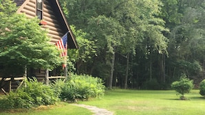 Een blokhut met een pad van stenen ervoor, omringd door weelderige begroeiing en een klein Amerikaanse vlag.
