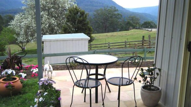 A patio with a table and chairs, surrounded by potted plants and flowers. - Fairmont Cottage (Woodhill)
