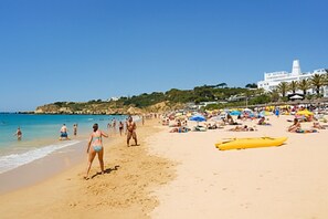 A crowded beach with people sunbathing and swimming, a white building in the background, and a yellow kayak on the sand.