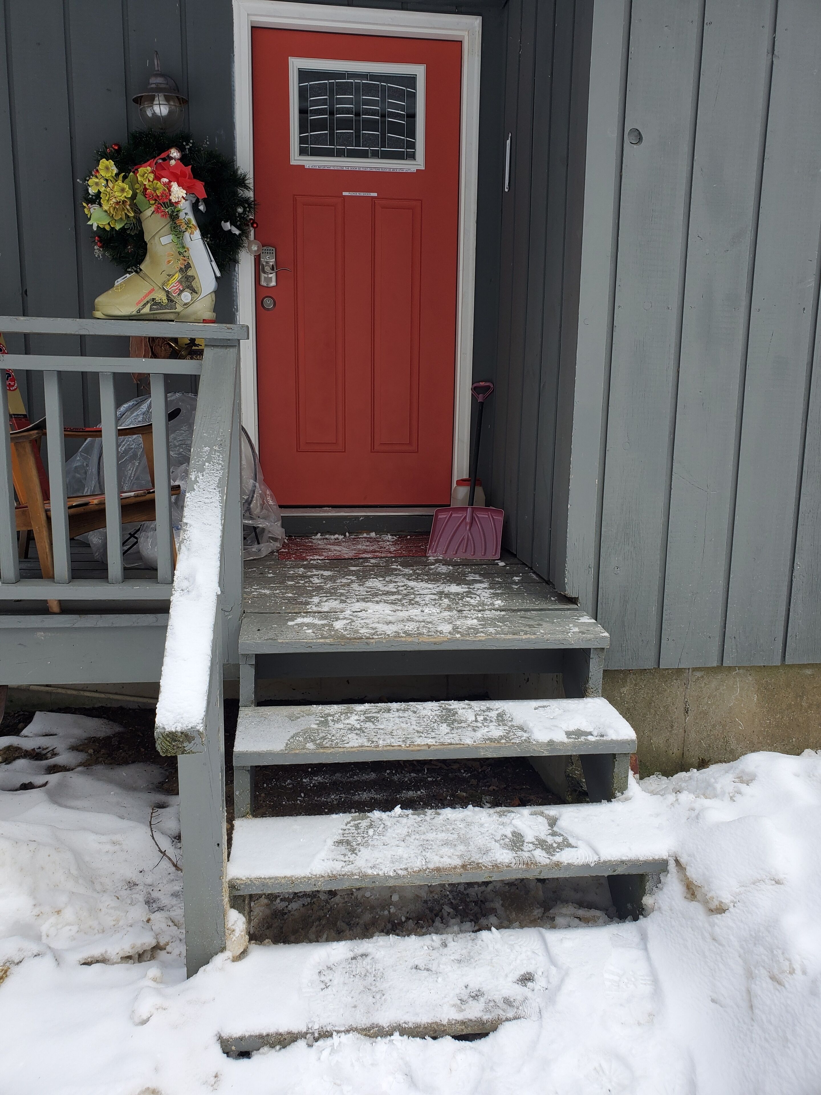 A red door with a window, a porch with steps, and a snow-covered ground.