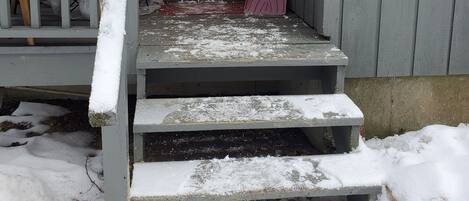 A red door with a window, a porch with steps, and a snow-covered ground.