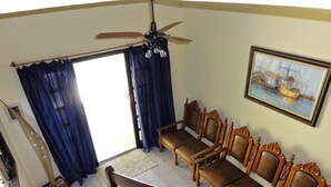 Una habitación con ventilador de techo, un conjunto de sofás, un cuadro y una ventana con cortinas.