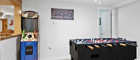 Una habitación con mesa de futbolín, juke box y televisor montado en la pared.
