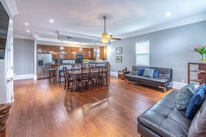 A spacious living room with hardwood flooring, a leather sofa, and a dining area with wooden chairs and a central island.