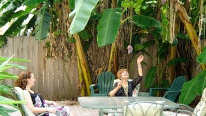 Two people sitting at a round table in a garden with chairs and a wooden fence in the background. - Garden District Upscale Escape w/Gated Off-St Parking & Streetcar Access (New Orleans)