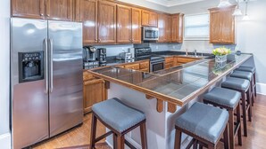 A modern kitchen with wooden cabinets, stainless steel appliances, a central island with bar stools, and pendant lighting. - Garden District Upscale Escape w/Gated Off-St Parking & Streetcar Access (New Orleans)