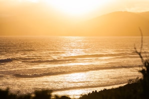 A sunset over a body of water with waves and a silhouette of a mountain in the background.