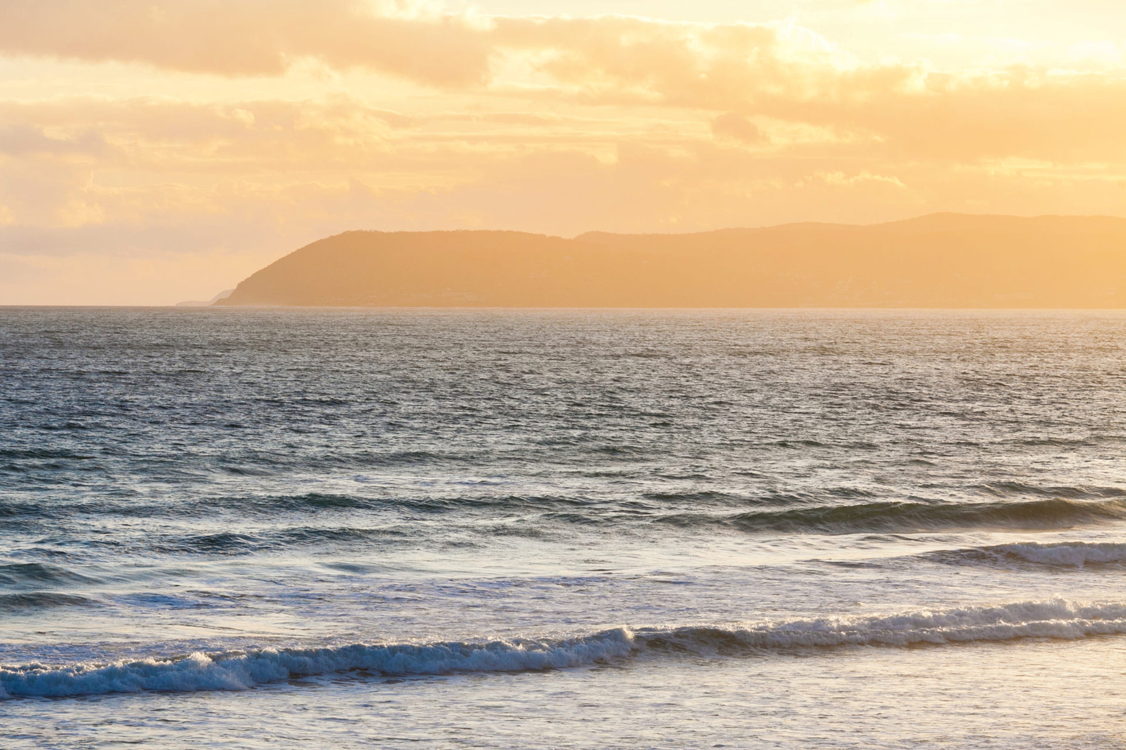 A coastal view with waves and a distant mountain range.
