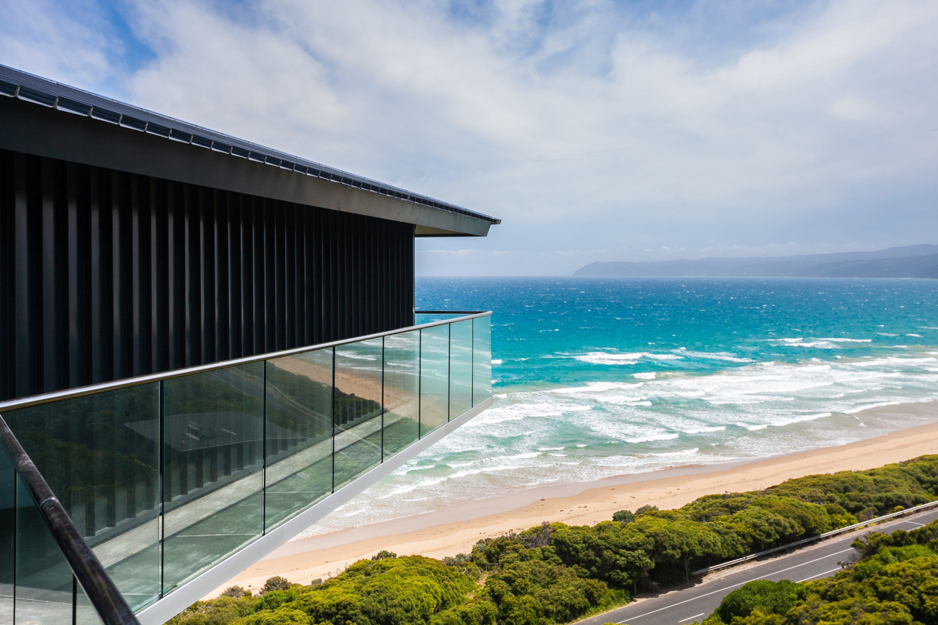 A modern building with a glass facade overlooking a beach and the ocean.