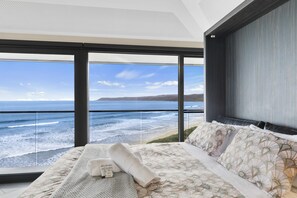 A bedroom with a large window overlooking the ocean, a bed with a patterned bedspread, and a neatly folded towel.