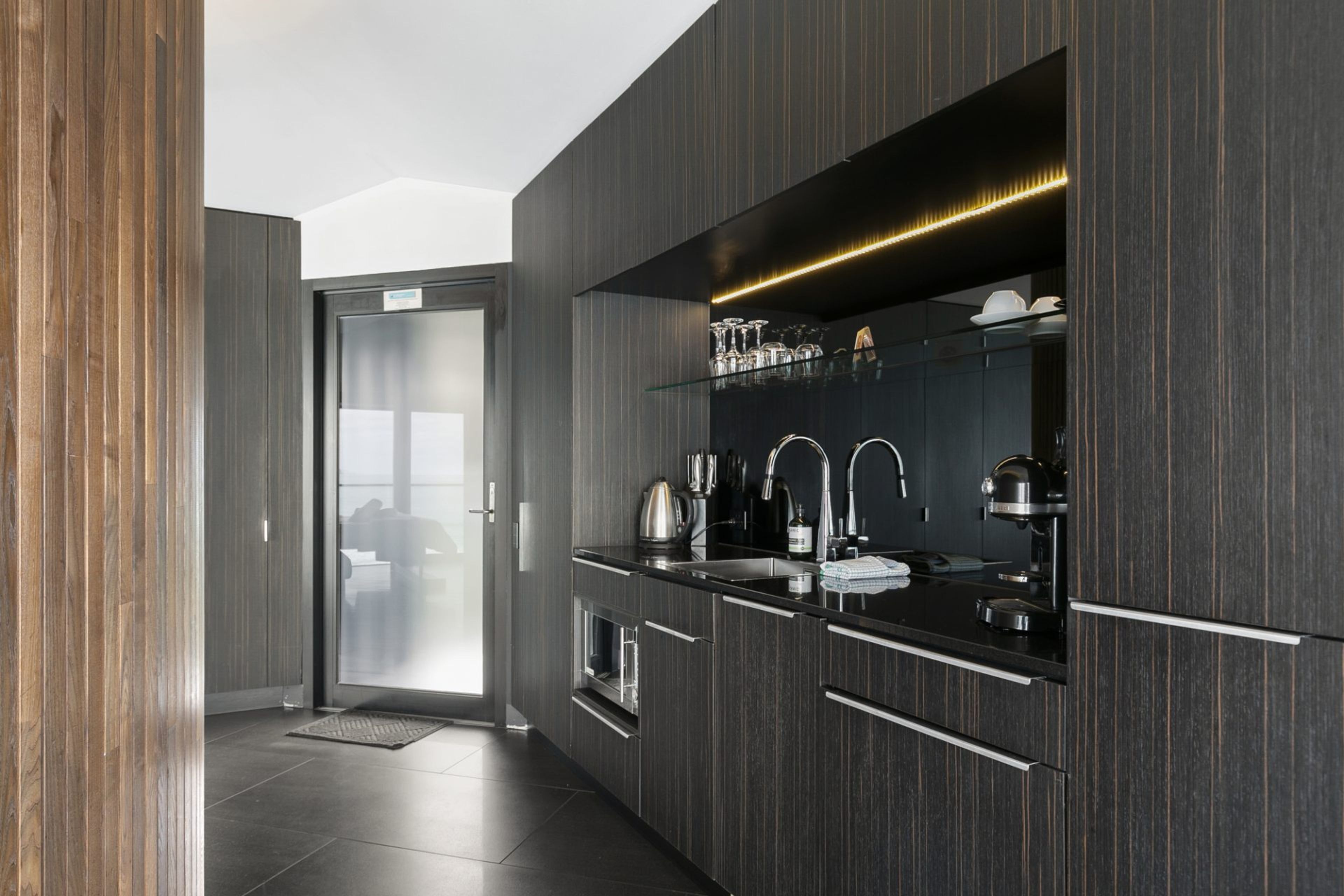 A modern kitchen with dark wood cabinetry, stainless steel appliances, and a glass door leading to another room.