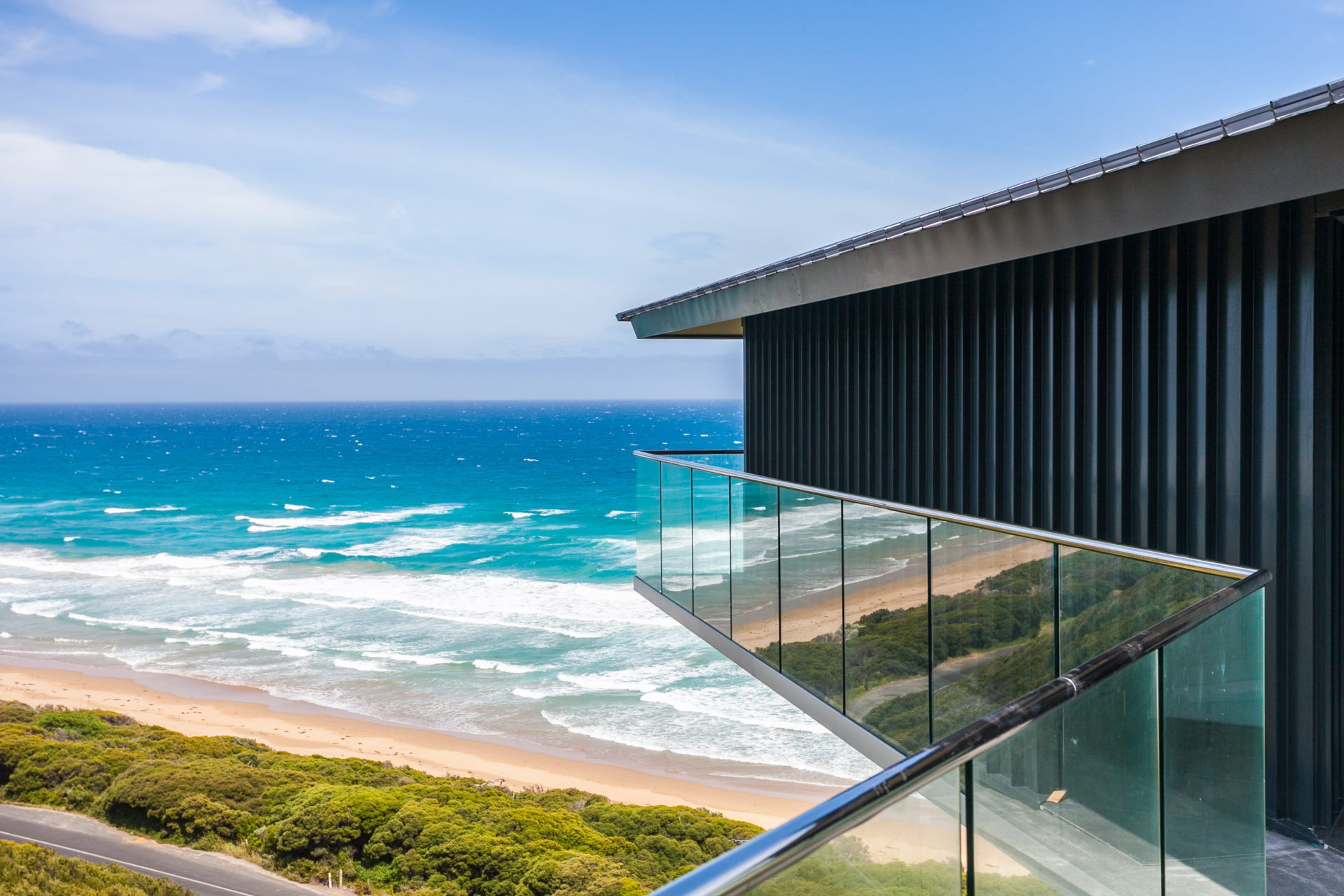 A modern building with a glass balcony overlooking a beach and ocean.