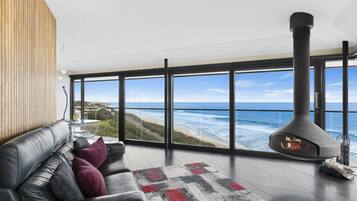 A modern living room with a leather sofa, a patterned rug, and a large window overlooking a beach and ocean.