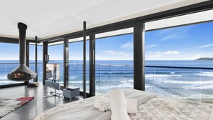 A modern room with a large window overlooking the ocean, a fireplace, a flat-screen TV, and a neatly made bed.
