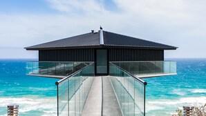 A modern structure with a glass walkway leading to a rooftop, overlooking a body of water.
