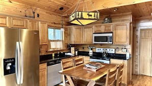 Cocina de cabaña de madera con un refrigerador de acero inoxidable, un microondas, una estufa y una mesa de comedor de madera con sillas.