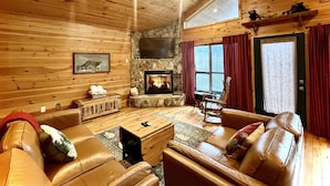 Interior acogedor de una cabaña con chimenea, sofás de cuero y una pared de piedra.