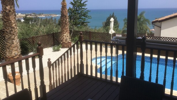 Un espace piscine doté d’une terrasse en bois, de palmiers et offrant une vue sur la mer.