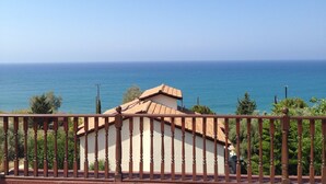 Un bâtiment situé sur la côte, doté d’un toit en tuiles, entouré de verdure et offrant une vue dégagée sur la mer.