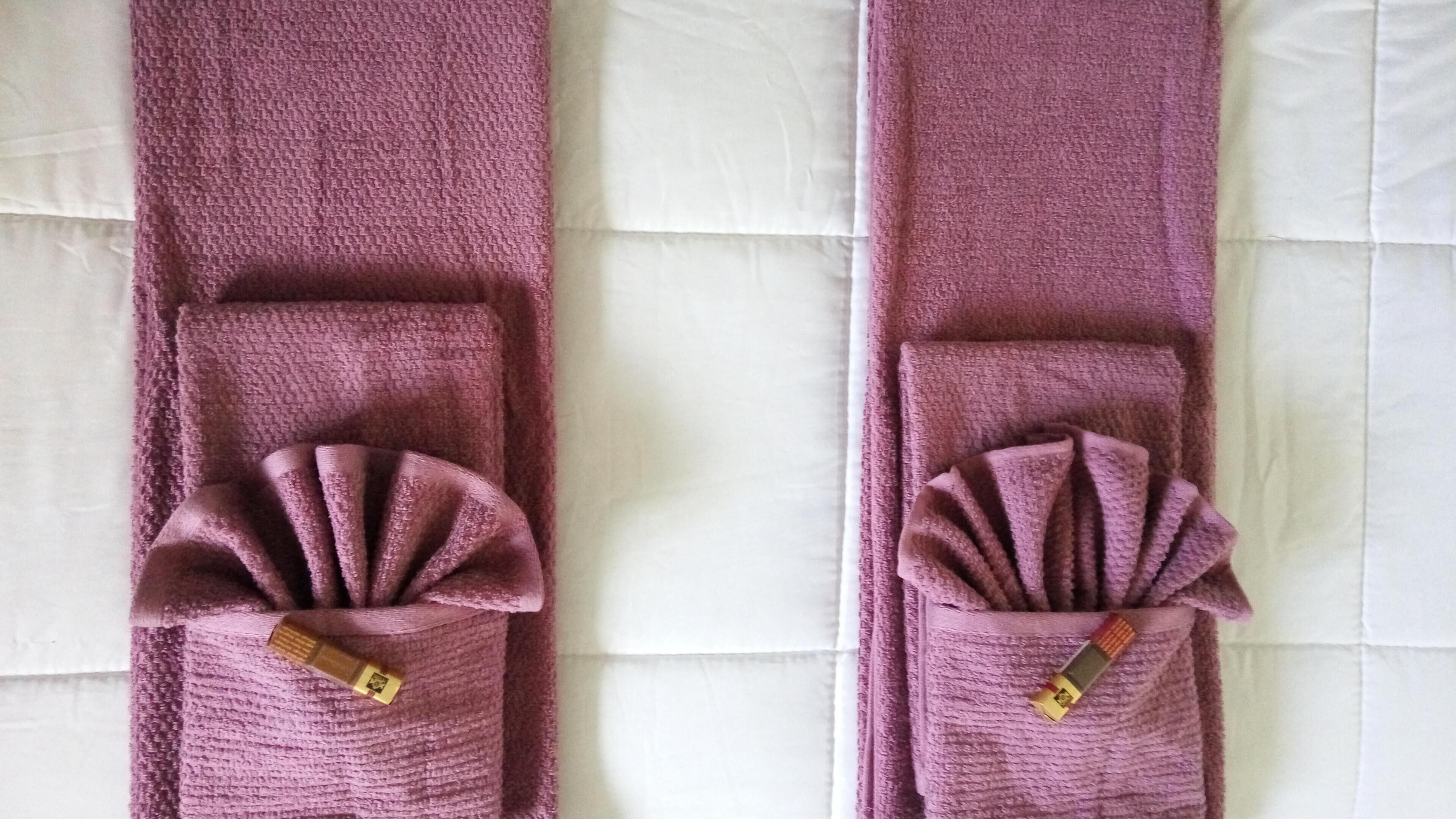 Two purple towels with decorative folds and a gold tag, placed on a white bedspread.