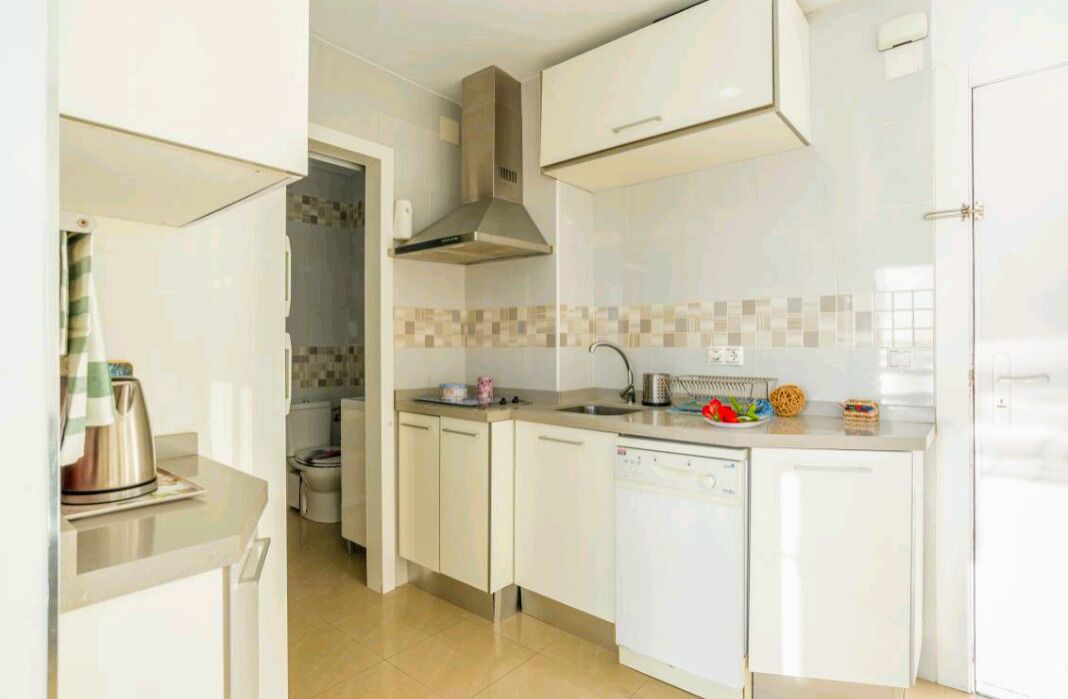 Una cocina moderna con armarios blancos, una campana extractora de acero inoxidable y lavavajillas.