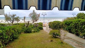 Une vue depuis un espace abrité donnant sur une plage, avec un sentier menant à la mer.