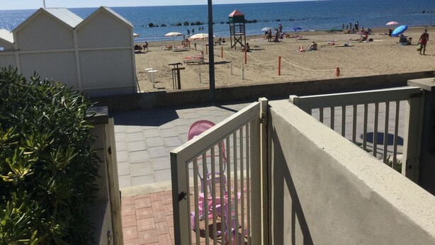 Une vue sur la plage, avec un ciel dégagé, une tour de surveillance des sauveteurs, des parasols et des chaises de plage.