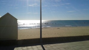 Une vue sur la plage, avec un ciel dégagé, une plage de sable et un petit bâtiment.
