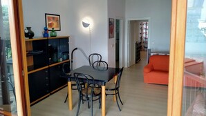 Un coin repas avec une table et des chaises, un meuble avec des étagères, une lampe fixée au mur et une porte donnant sur une autre pièce.