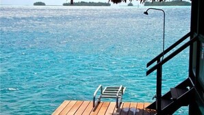Un pontile in legno che si estende sull'acqua turchese, con una ringhiera in metallo e una sola sedia in metallo.