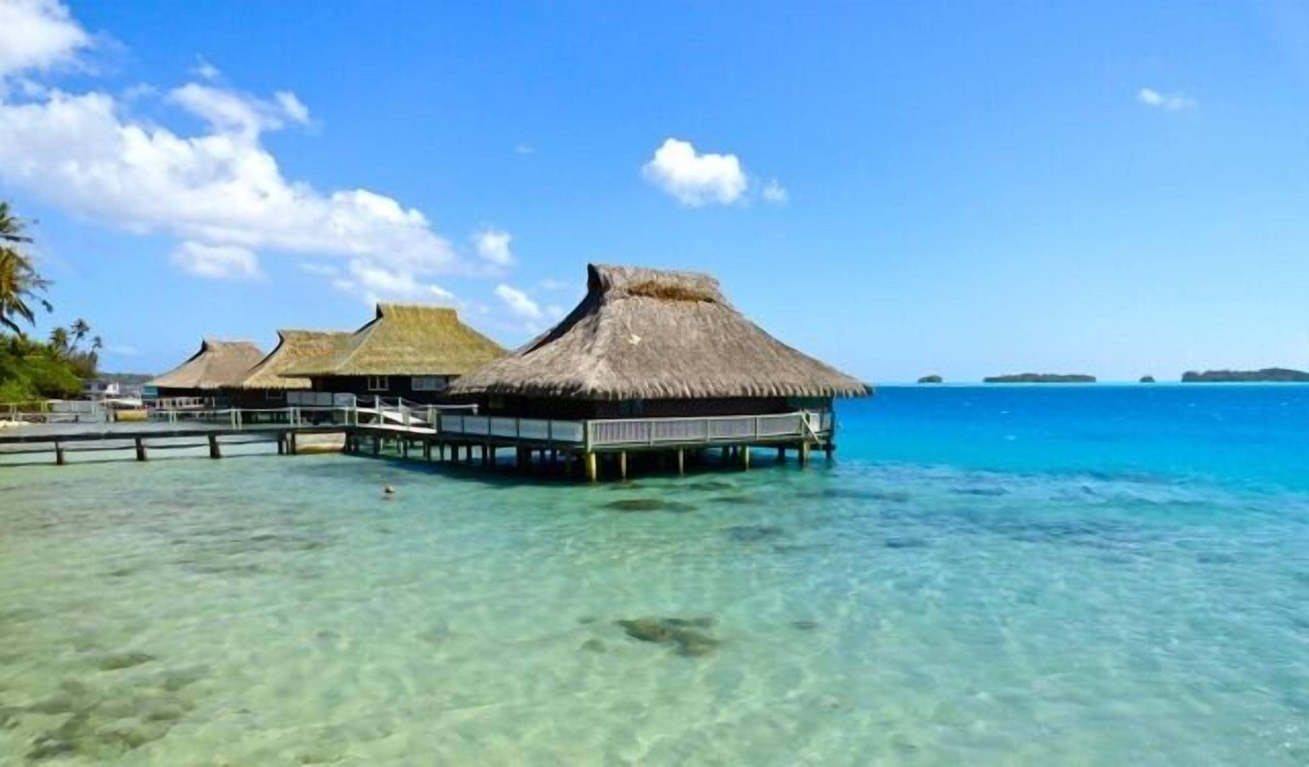 Des bungalows sur pilotis, dotés de toits de chaume et de passerelles en bois s’étendant dans des eaux turquoise et cristallines.