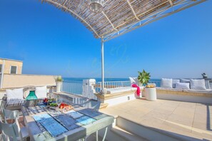 Une terrasse sur le toit avec une table dressée pour le dîner, un coin salon avec des coussins et une vue sur la mer.