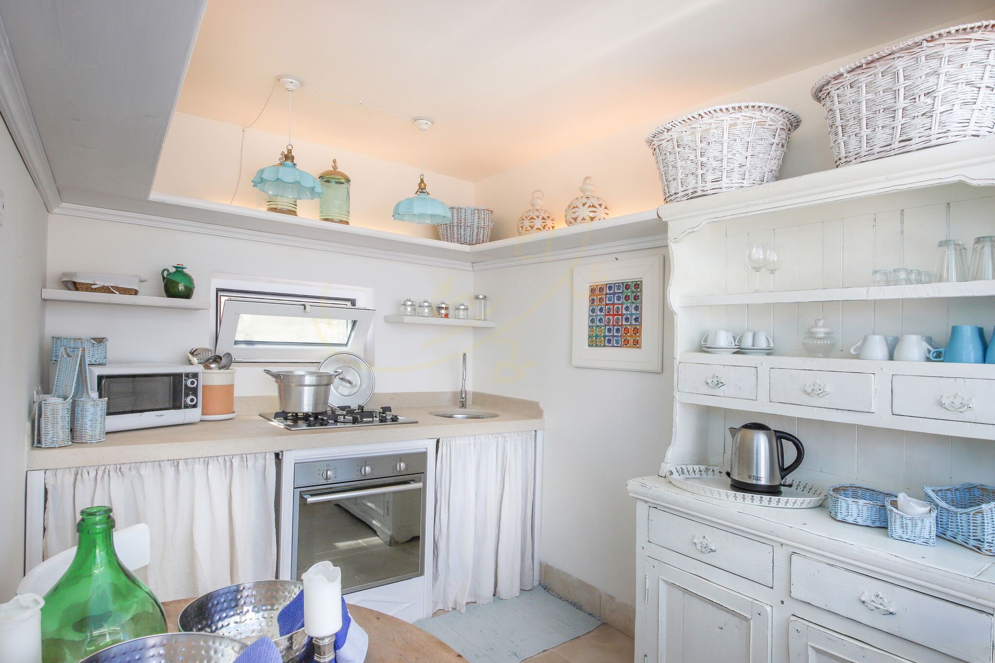 A compact kitchen with a microwave, stove, oven, and various kitchenware on shelves and counters.