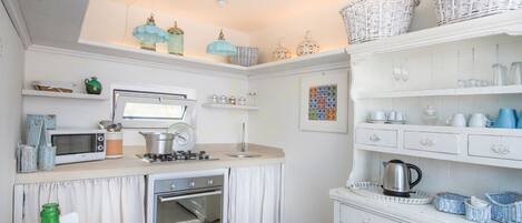 A compact kitchen with a microwave, stove, oven, and various kitchenware on shelves and counters.