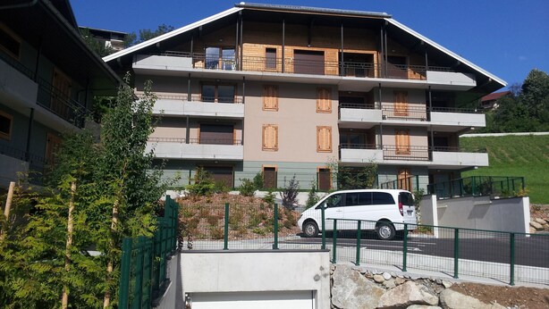 A multi-story building with balconies, a car parked in front, and a green fence. - Superb new apartment, nice and functional. Heartwarming welcome.  (Saint-Gervais-Les-Bains)